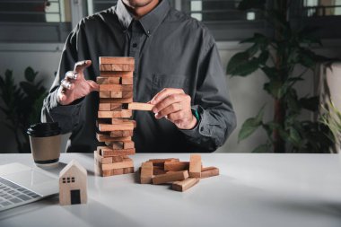 Alternatif risk planı. İş adamı kule blokları oyunu oynuyor, adam bir tahta bloğu kuleden çekiyor yumruğunu sıkıyor, bunu başarmaktan büyük keyif alıyor, iş büyütme konsepti.