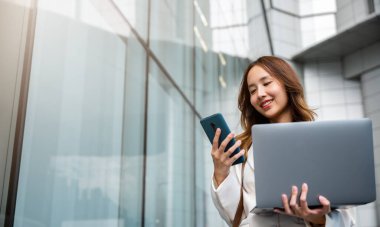 Kendine güvenen iş kadını şehirde duran bilgisayarlı akıllı telefonu kullanıyor. Güzel iş kadını çalışmaya hazır. İş konsepti.