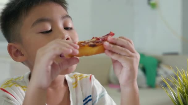 快乐的亚洲小男孩5年坐在家里桌上吃着巨大的比萨饼 孩子们吃着不健康的食物 兴奋有趣的孩子吃着比萨饼 吃着早餐 吃着奶酪 好吃地吃着许多片 — 图库视频影像