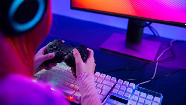 Gamer using joystick controller for virtual tournament plays online video game with computer neon lights, woman wear gaming headphones playing live stream esports games console at home