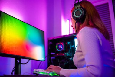 Oyun kulaklığı takan Asyalı kadın oyuncu video oyunu oynamak için joystick konsolu tutuyor ve evdeki bilgisayar PC neon ışığı ile çevrimiçi yayın yapıyor, turnuva oyuncusu E-Sport konsepti