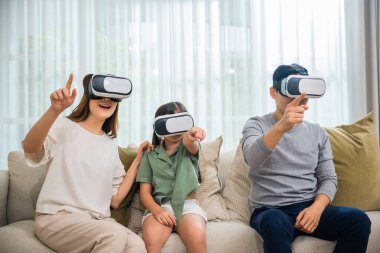Happy family have mother father and daughter watching movie or playing video game, Asian family wear vr glasses headsets fun sitting on sofa in living room, game entertainment innovation technology