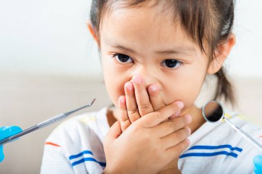 Dişçi çocuk muayenesi. Doktor ağız boşluğunu muayene ediyor diş boşluğunu kontrol etmek için ağız aynası kullanıyor ama küçük kız ağzını kapatıyor kontrol etmeye gerek yok korkmuş, korkmuş ve elleriyle ağzını kapatıyor.