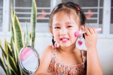 Mutlu çocuk güzel makyaj oyuncağı, Asyalı sevimli komik küçük kız makyaj yapıyor aynaya ve yanak fırçasına bakıyor pudra için, kadın olmayı öğreniyor.