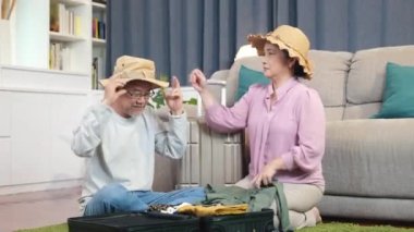 Asyalı, emekli, elbiseli, seyahat çantalı, ev içi oturma odasının zemininde bir çift yaşlı, evli, emekli, seyahat için hazırlanan valizleri hazırlayın.