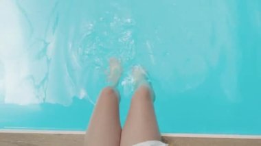 Beautiful sporty slim woman legs relaxing in water swimming pool spa, Enjoying suntan summer time, Female splashing feet in turquoise blue waters, Vacation feeling concept, Top view