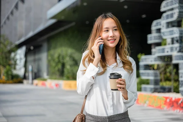 一个漂亮的女人走在外面的街上 在办公室附近用手机打电话 一边拿着咖啡杯 一边向顾客展示一个带着手提包的女商人的形象 — 图库照片