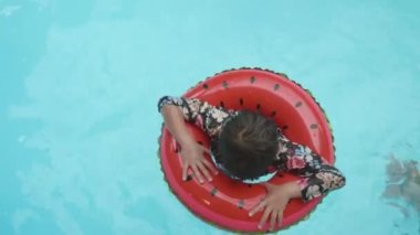 Yaz çocuğu Aquapark 'ta rahatla. Lastik yüzüklü mutlu Asyalı çocuk havuzda mavi suda yüzüyor tatil köyünde eğleniyor, yaz tatili konsepti, üst manzara