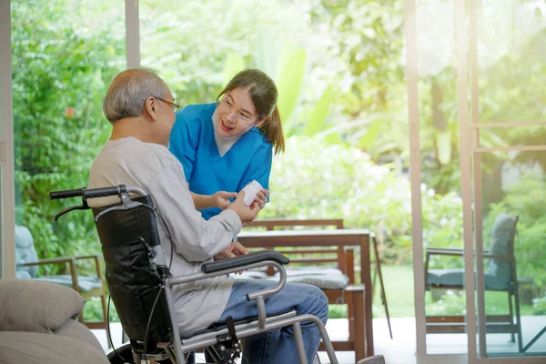 当老年老年男性病人有时间回家护理家庭时 亚洲年轻女性在帮助下提供的护理药丸为坐轮椅的老年残疾病人开药方 医药和保健 — 图库照片