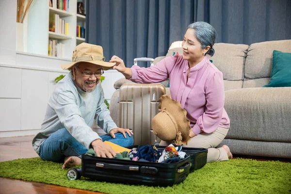 アジアカップル古いシニア結婚退職準備荷物スーツケース手配旅行 ロマンチックな退職したカップルの梱包服旅行バッグスーツケース一緒に床の上に家のインテリアリビングルーム — ストック写真