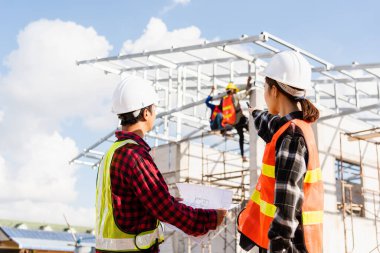 İki mimar ve müvekkil inşaat alanındaki planların oluşturulmasına yardım ediyor. Asyalı mühendis ustabaşı kadın ve erkek kağıt projesi hakkında konuşuyor.