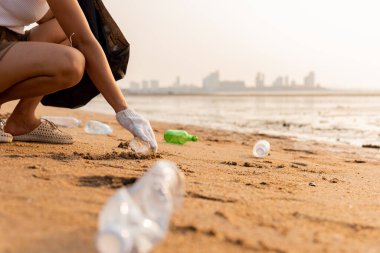 Plajı temizlemek için plastik poşet içine plastik şişe karıştıran gönüllü bir kadın, çöpleri temizleyen bir kadın, ekoloji konsepti ve Dünya Çevre Günü, Dünya 'yı Kurtarma Günü.