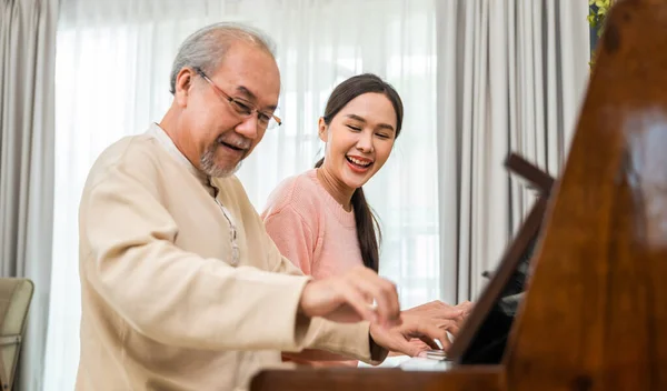 年轻女子为老人教钢琴 快乐的女儿和年老的父亲带着眼镜放松地一起在客厅里弹钢琴 退休后的生活 — 图库照片