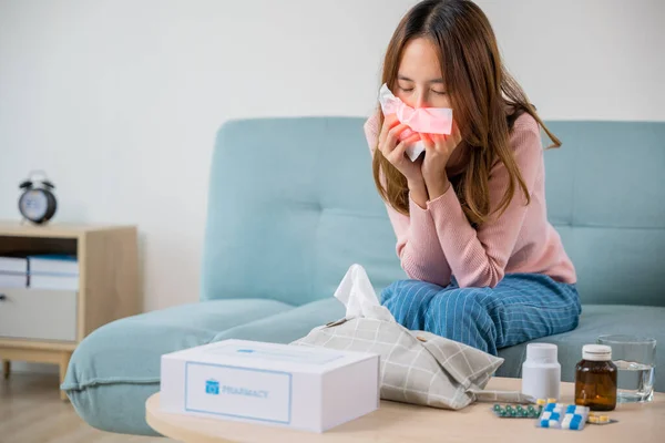 Sick woman. Beautiful female health problem blowing nose use pharmacy kit box delivery service from hospital, delivery pharmacy concept, Asian young girl cold sick she sneeze with tissue paper on sofa