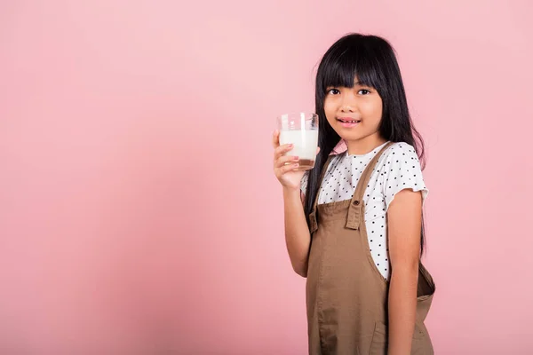 Asian little kid 10 years old smile hold milk glass drink white milk at studio shot isolated on pink background, Happy child girl daily life health care Medicine food