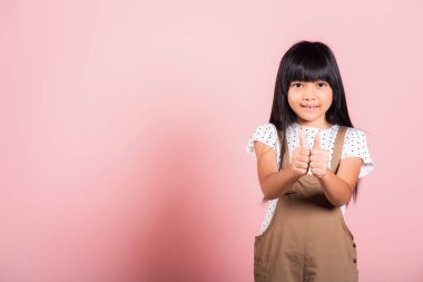 Asyalı küçük bir çocuk, 10 yaşında pembe arka planda izole edilmiş bir şekilde stüdyoda baş parmak gösteriyor mutlu çocuk portresi güzel bir jest için gülümsüyor.