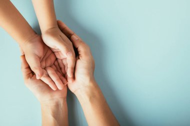 Üst düzey ebeveynler ve küçük çocuklar el ele tutuşuyorlar. Stüdyo çekimleri mavi arka planda, aile evinde izole edilmiş, çocukları yetişkin annelerin eline teslim ediyor, destek oluyor, aile günü kavramına destek oluyor.