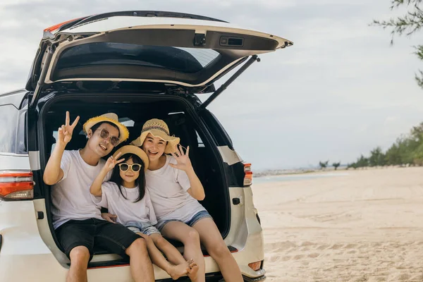 Tourism Day. Parents and children family traveling in holiday at sea beach show V-sign finger. Dad, mom and daughter enjoying road trip sit on back car. family having fun in summer vacation on beach