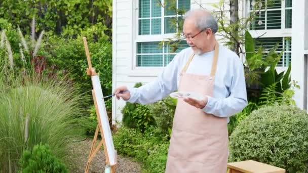 亚洲老年人用画笔和油画在画布上画图画 老年人在绿色自然的背景外对画架微笑 快乐退休的艺术家活动 — 图库视频影像
