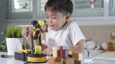 Çocuk tamir etmeyi öğreniyor. Ders kontrol robotu kolu alıyor. Mutlu Asyalı çocuk, evde robotik makine kolu tamir etmek için tornavida kullanıyor.