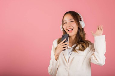 Bluetooth kulaklıkla müzik radyosu dinlerken ve akıllı telefon stüdyosunda şarkı söylerken heyecanlanan kadın izole edilmiş pembe arka plan, mutlu Asyalı genç bayan Karaoke çevrimiçi cep telefonu uygulaması