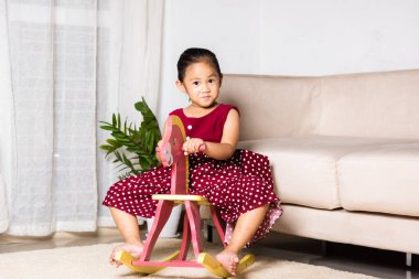 Asyalı şirin küçük kız oyuncak ata biniyor, gülümseyen çocuk evde sallanan sandalye oynuyor anaokulunda oynamak için mutlu zamanlar.