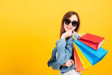 Asyalı mutlu portre güzel sevimli genç kız güneş gözlükleriyle gülümsüyor alışveriş çantaları tutarken heyecanlanıyor çok renkli kameralar izole edilmiş, stüdyo sarı arkaplan ve fotokopi alanı