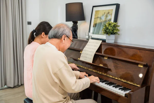 Family care. Asian young woman teaching piano for senior man teaching, happy daughter and elderly father playing the piano together in living room at home, lifestyle life after retirement