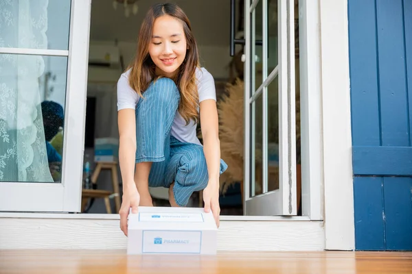 Close up hands of sick Asian woman sitting at door to receive medication first aid pharmacy box package from hospital delivery service at floor home, drugstore internet online medical business