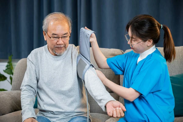 Asian nurse visit patient senior man at home she measuring arterial blood pressure on arm in living room, Doctor woman examine do checking old man client heart rate with pulsimeter monitor, Healthcare