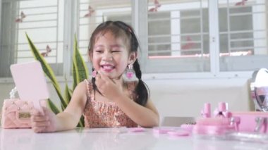 Asyalı sevimli küçük kız makyaj yapıyor ve aynada kendine bakıyor, kadın olmayı öğreniyor, mutlu çocuk güzel bir makyaj oyuncağı.