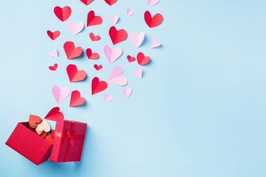 Valentines day background. Red gift box postcard and paper flying elements hearts cut greeting gift card isolated on blue background, Symbol of love. Top View Happy Mothers, Valentines Day concept