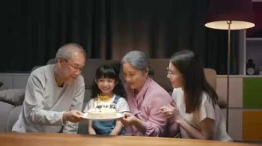 Mutlu Asyalı aile büyükbabaları ve anneleri doğum günü partisinin tadını çıkarıyor. Torunlarının pastasıyla evde mum üflüyorlar. Doğum günü sürprizi konsepti.
