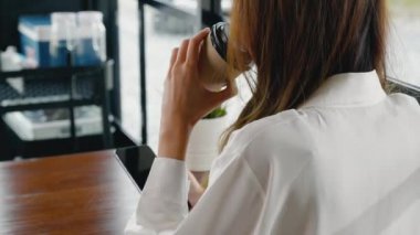 Güzel, genç bir iş kadını, dışarıda öğle yemeği, kafeteryada akıllı telefon ve kahve kağıdı tutuyor, kafeteryada mutlu bir kadın hayatı yaşıyor, pencerenin yanında oturuyor, cep telefonu kullanıyor.