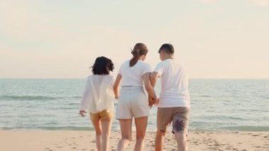 Mutlu arkadaşlar el ele tutuşup hayatın tadını çıkarıyorlar kumsalda birlikte özgürlüğün tadını çıkarıyorlar gün batımında tatil tatilinde genç Asyalı kadın ve erkek yaz seyahatinde, insanların yaşam tarzı