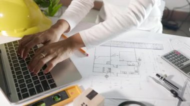 Mimari proje işyeri. Mimarlık bürosundaki masa başı masa üzerinde cetvel üzerinde cetvel çizmeden ya da taslak çizmeden önce evin tasarımını gözden geçirmek için dizüstü bilgisayar klavyesi yazmayı seçin