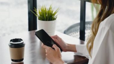 Güzel, genç bir iş kadını, dışarıda öğle yemeği, kafeteryada akıllı telefon ve kahve kağıdı tutuyor, kafeteryada mutlu bir kadın hayatı yaşıyor, pencerenin yanında oturuyor, cep telefonu kullanıyor.