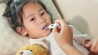 Hasta çocuk. Anne babası hasta kızının sıcaklığını kontrol ediyor. Ağzı dijital termometreyle, çocuk yatakta yatıp ateşini ve hastalığını ölçüyor.