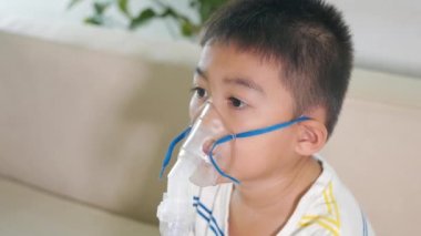 Asian Child using nebulizer mask equipment alone have smoke, Kid boy making makes inhalation nebulizer steam sick cough at home, oxygen spray inhaler therapy, stuffy nose and runny, Health medical