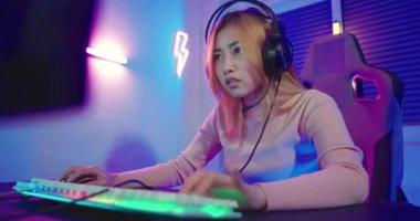 Young player woman wearing gaming headphones intend to do playing live stream games online at home, Happy Gamer endeavor plays online video games tournament with computer desktop with neon lights