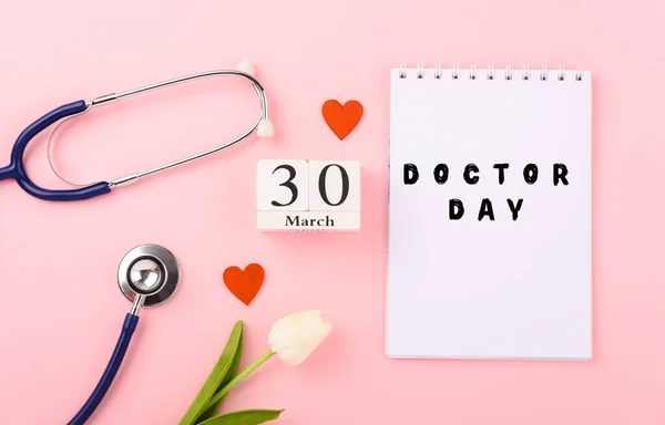 Doctor Day Concept, Top view of medical red heart tulip flowers and doctor stethoscope with white note book on pink background, care patient in hospital with copy space, Medical and Healthcare