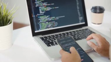 Software developer hands typing data coding programming javascript with laptop computer and mobile phone, Programmer woman looking smartphone program code at workplace, IT startup concept