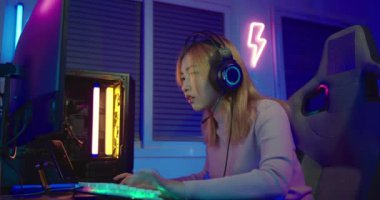 Zafer kazanmak. Asyalı oyuncu çevrimiçi video oyunu oynuyor. Masaüstü bilgisayarında heyecan verici PC renkli neon ışıklar, oyun kulaklığı takan genç kadın bilgisayarını kullanıyor. Başarılı, E-Sport konsepti.