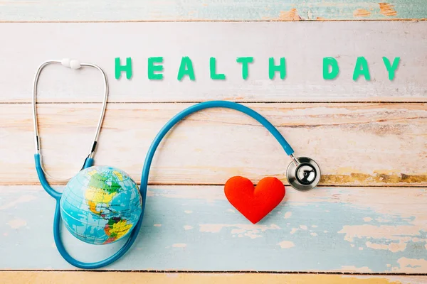 World Health Day. Yellow doctor stethoscope and world globe with Red heart shape on wooden background with copy space, Save world day, Green Earth Environment, Healthcare and medical concept