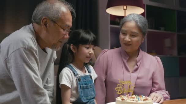 誕生日おめでとう 素晴らしいケーキを与えた後 彼の誕生日を祝いながら 家族の祖父と祖母は感謝の気持ちで孫娘を抱きしめています 自宅で子供とアジアのシニア家族パーティー — ストック動画