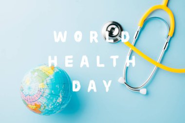 Dünya Sağlık Günü. Dünyanın dört bir yanındaki sarı doktor steteskobu pastel mavi arka planda izole edilmiş metin, küresel sağlık, sağlık ve tıbbi konsept için fotokopi alanı mevcut.
