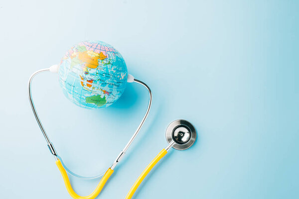World Health Day. Top view yellow doctor stethoscope wrapped around world globe isolated on pastel blue background with copy space for text, Save world day, Health care and medical concept
