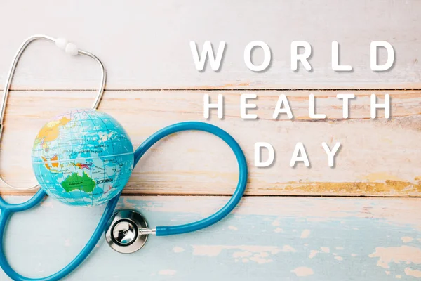 World Health Day. Blue doctor stethoscope and world globe isolated on wooden background with copy space for text, Save world day, Green Earth Environment, Healthcare and medical concept