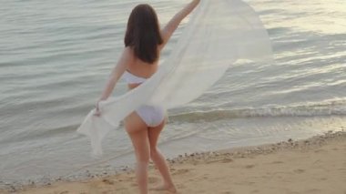 Genç ve güzel bir kadın bikini mayo giyip sarong üfleyerek tropikal plajda yürüyüş yapıyor ve vücut çeviriyor mutlu Asyalı seksi kadınlar dışarıda tatilde eğleniyor, yaz tatili tatilinde dinleniyor.