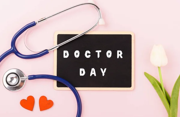 Doctor Day Concept, Above overhead of equipment medical red heart doctor stethoscope on pink background, care patient in hospital with black board and tulip flowers copy space, Medical and Healthcare